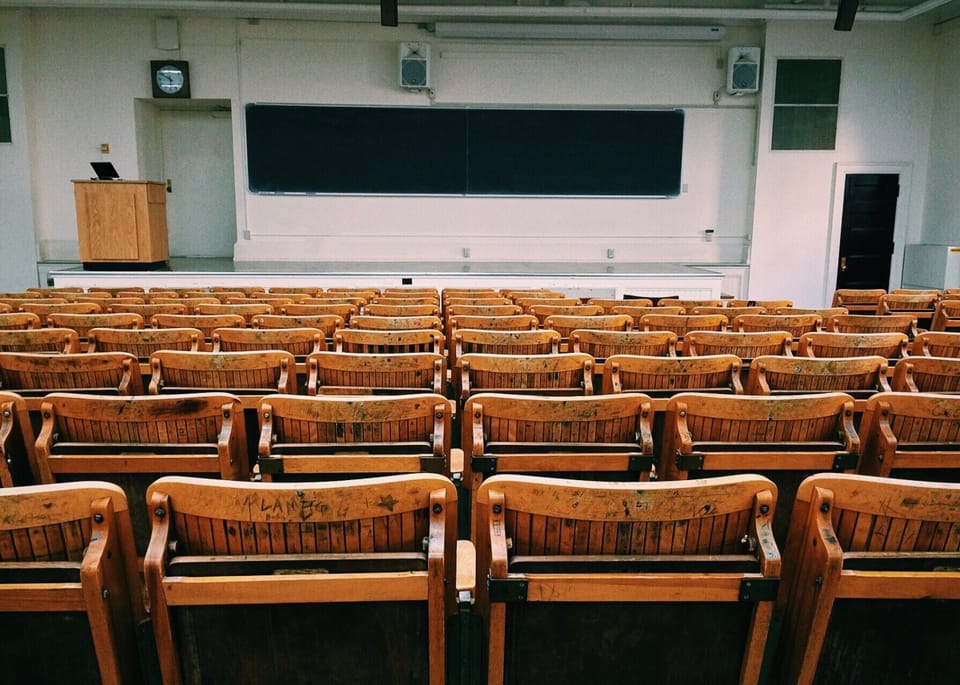Image of classroom with empty wood chairs facing white board and lecturer podium.