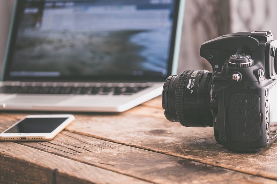 Image: DSLR camera, mobile phone and laptop sitting on a wood table.