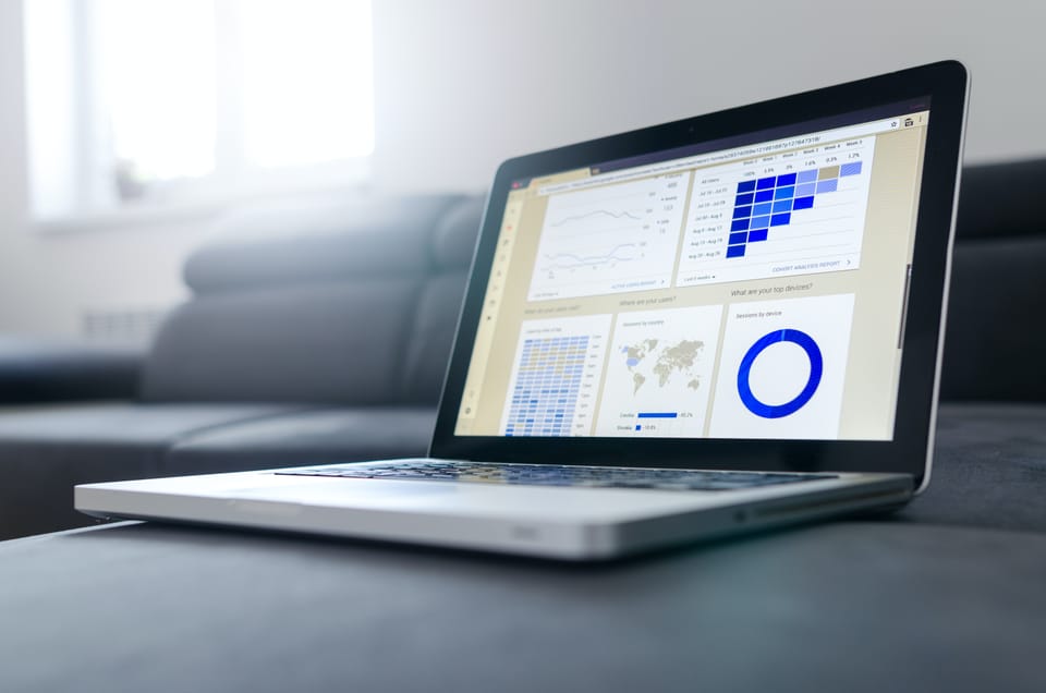 Image: laptop with blue data dashboard open on screen, sitting on a grey couch.